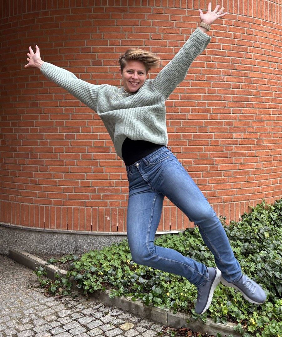 Leende kvinna som hoppar högt med utsträckta armar.