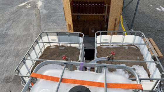 Stora vita plastkar med sand i. I bakgrunden ett träskåp med vertikala plaströr.