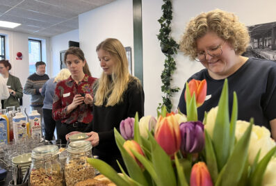 Tre kvinnor står leende vid en frukostbuffé, tulpaner i förgrunden.