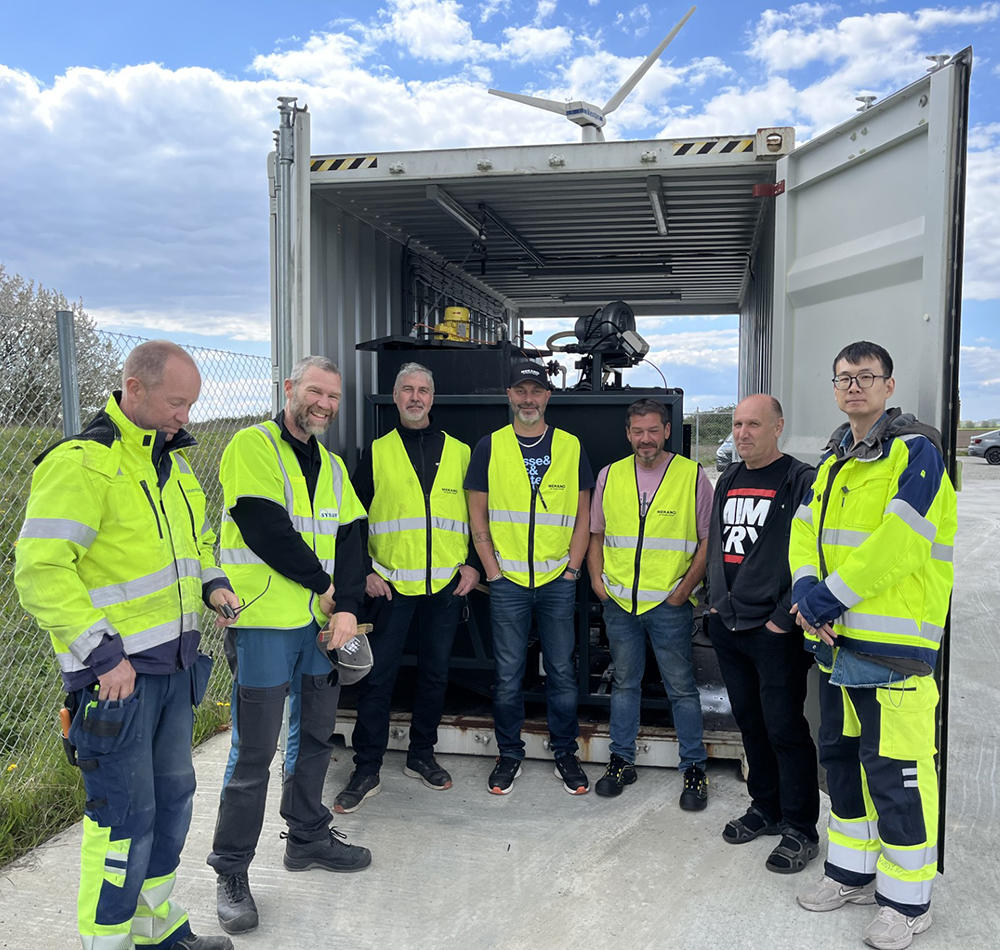 sju vuxna män i reflexväst framför en öppen container. 
