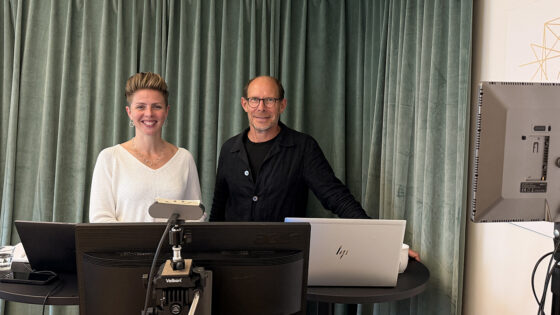 En kvinna och en man bredvid varandra i en studio. Skärmar och kamera.